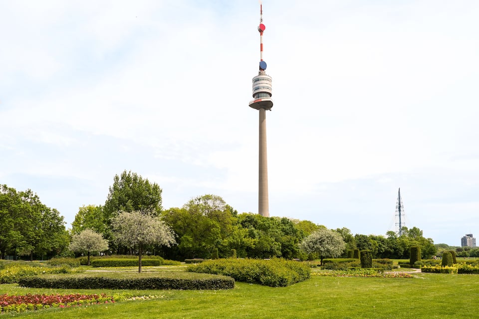 A tower with a red and white top, surrounded by a well-maintained park with various trees and flower beds.