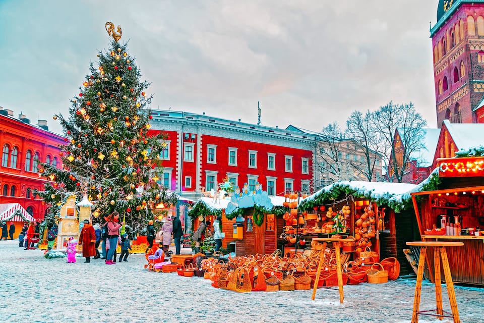 A snowy Christmas market with a decorated Christmas tree and traditional wooden stalls.