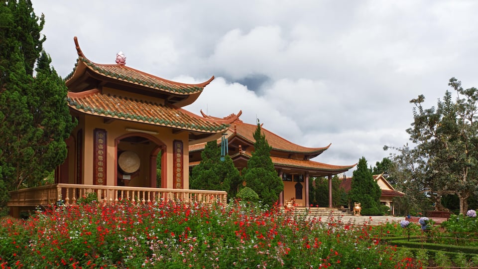 A traditional Chinese pavilion with ornate roofs and a garden with red flowers.