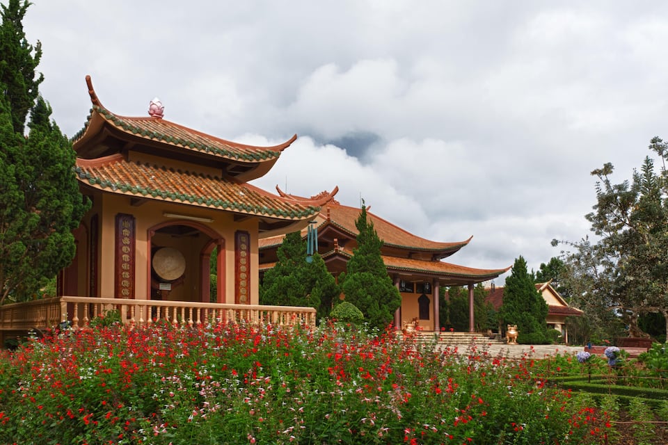 Ein traditioneller chinesischer Pavillon mit aufwendigen Dächern und ein Garten mit roten Blüten.