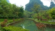 A serene river meandering through a lush park with dense greenery and a distant mountain backdrop.