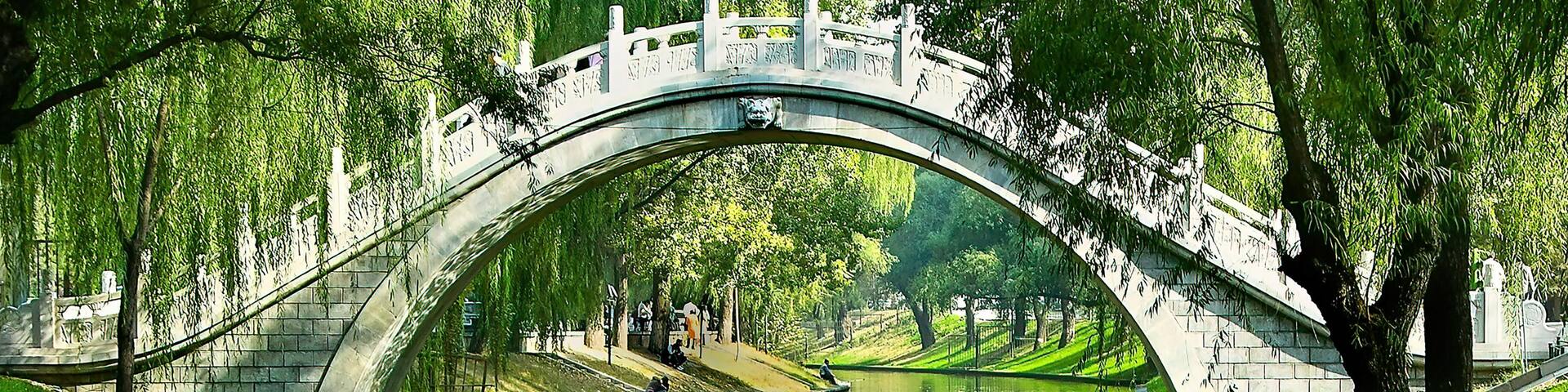Un puente de piedra sobre un canal, con reflejos de árboles y un cielo despejado.