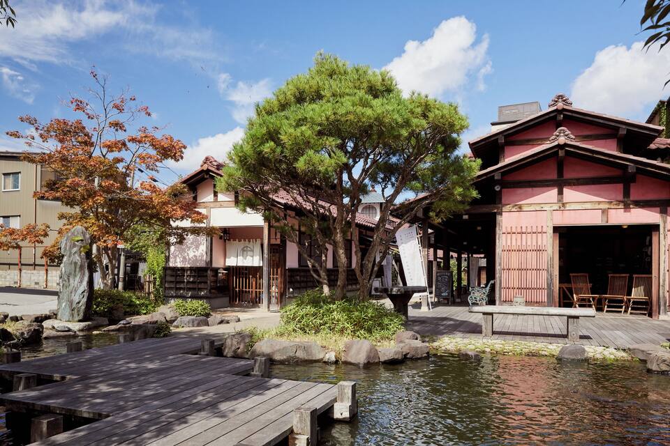 A traditional Japanese garden with a wooden bridge, a pond, and a large tree.