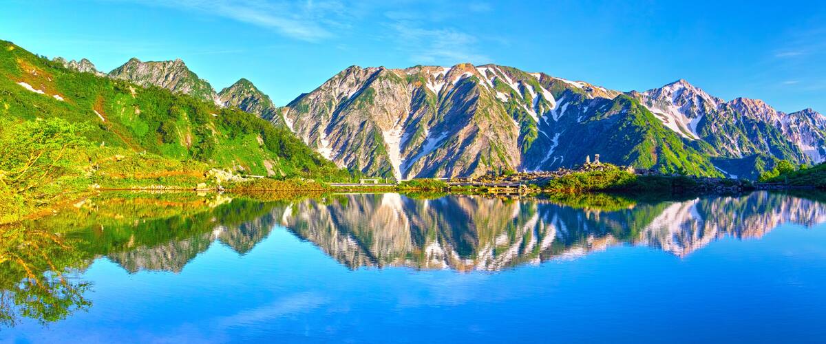 A mountain lake with reflections, green hills, and a small building.