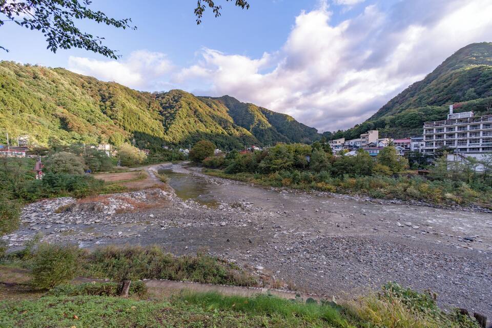 A river flowing through a valley with mountains in the background and buildings along the riverbank.
