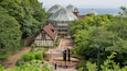 A garden with a glass greenhouse, a traditional building, and a view of the sea.