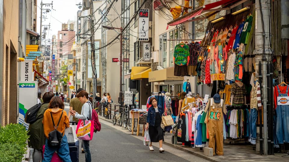 Uma rua movimentada com pedestres, bancas de roupa e diversos anúncios.