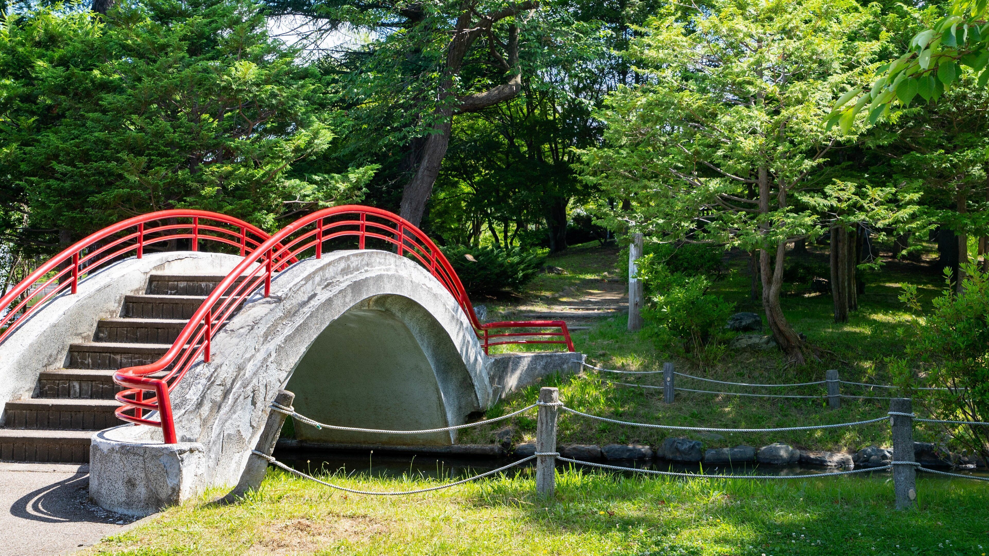 A stone bridge with red railings in a park.