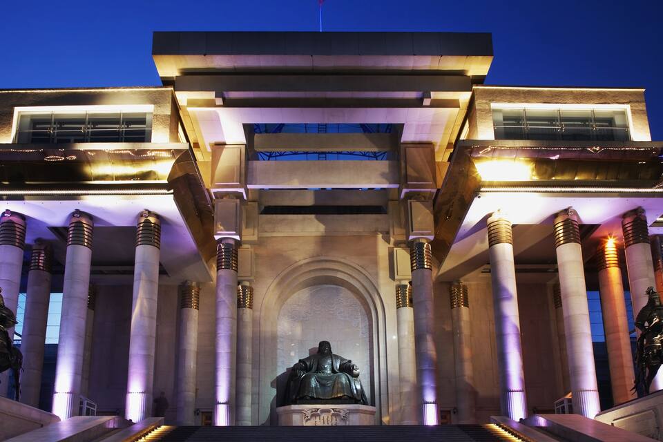Una entrada imponente con una estatua, columnas monumentales y arquitectura iluminada.