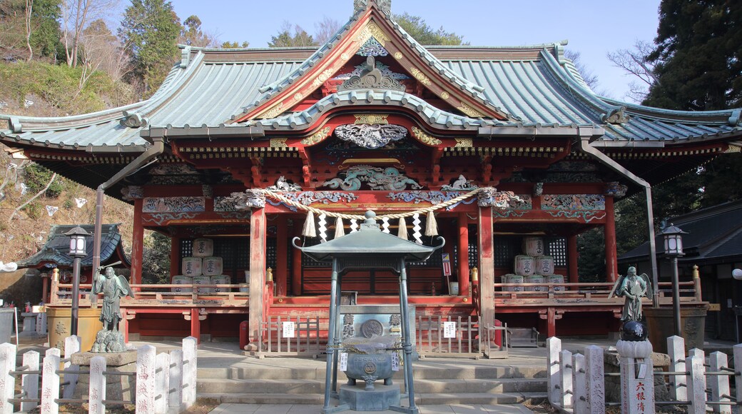 Un templo japonés tradicional con arquitectura ornamentada, una estatua central y piedras conmemorativas.