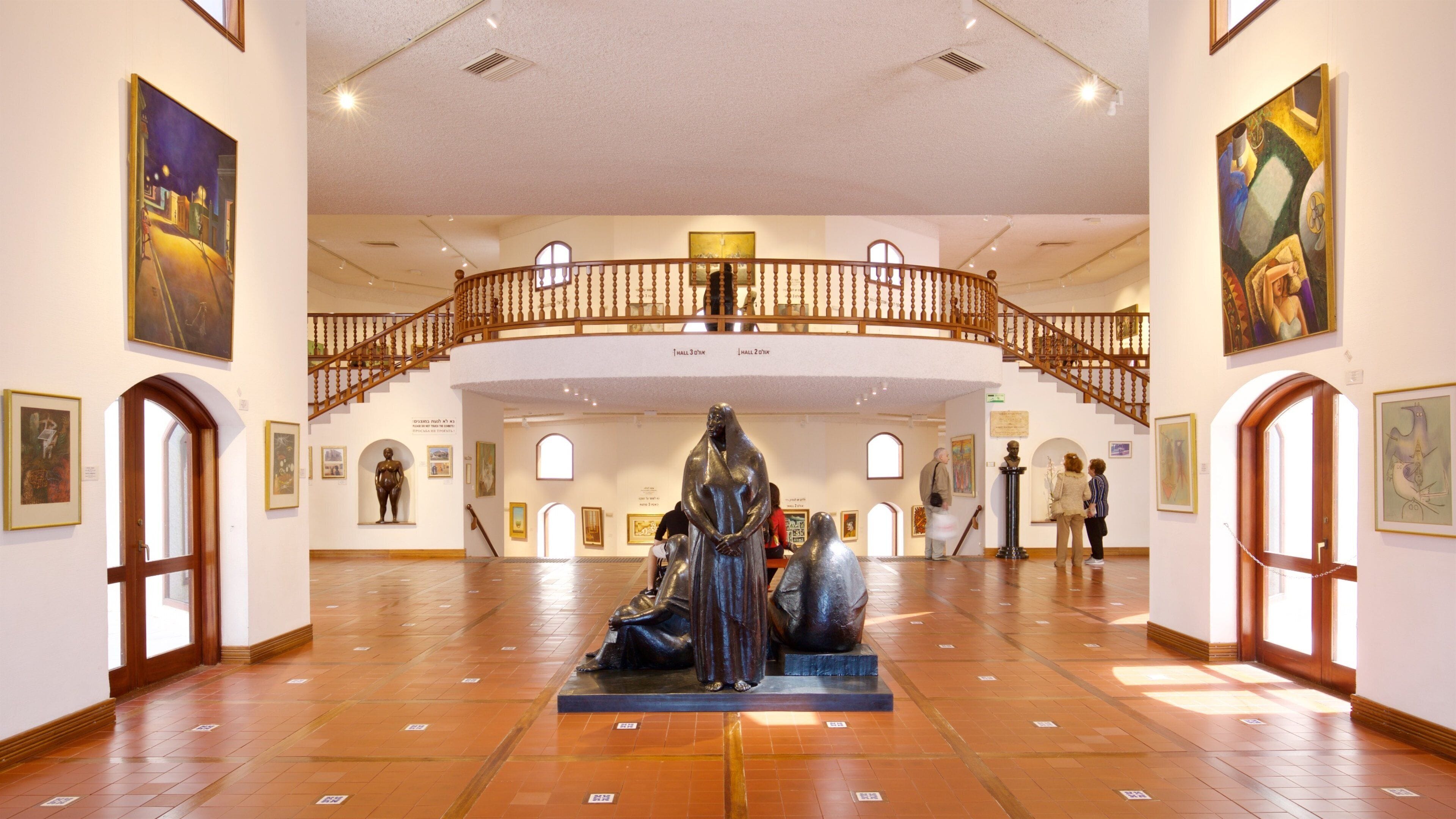 An art gallery with a central sculpture, wooden railings, and various paintings on the walls.