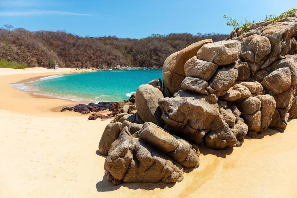 A sandy beach with large rocks and a clear blue sea.