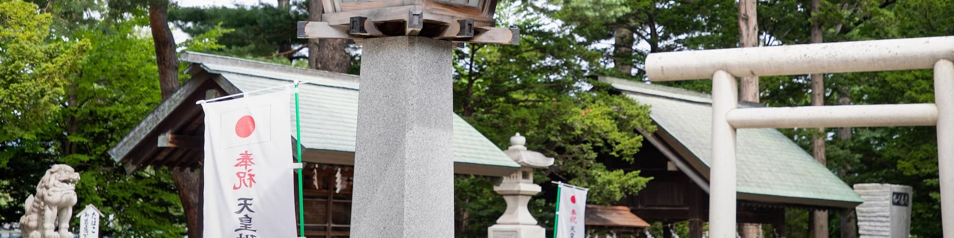 A traditional Japanese torii gate with a stone lantern in front, surrounded by lush greenery and a pagoda in the background.