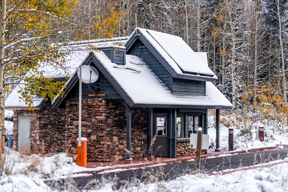 Una casa in pietra con tetto spiovente e un piccolo portico, circondata da alberi imbiancati dalla neve e da un bosco.