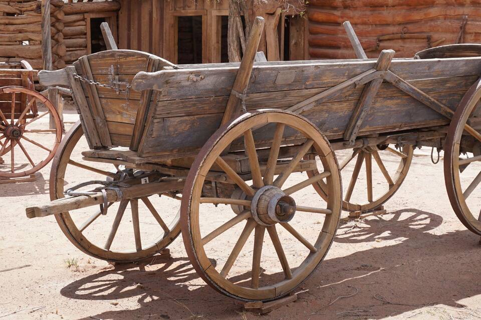 An old wooden wagon with large wooden wheels, positioned in front of a rustic log cabin.