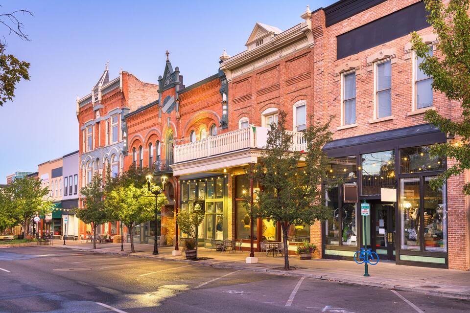A historic street lined with brick buildings, outdoor seating, and trees.