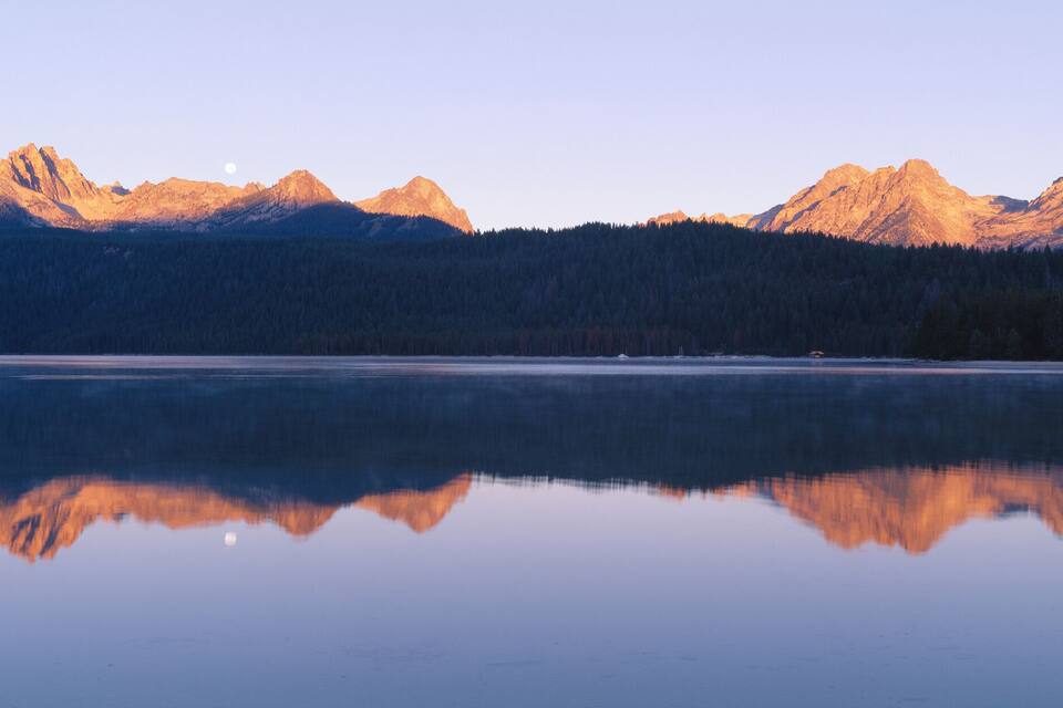 A mountain range reflected in a calm lake with clear skies.