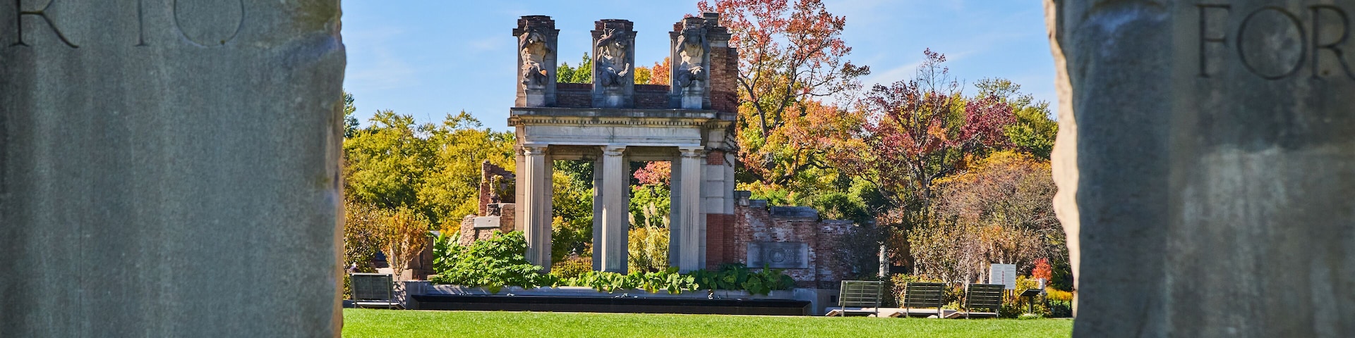 View through two stone obelisks of old stone and brick ruins in park