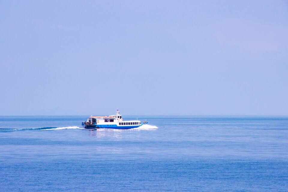 Un bateau bleu et blanc navigue sur des eaux calmes et bleues, sous un ciel dégagé.