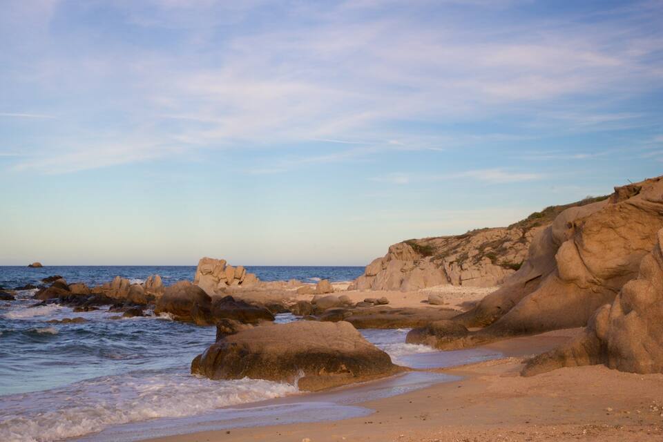 A rocky coastline with waves crashing onto the shore and a clear sky.