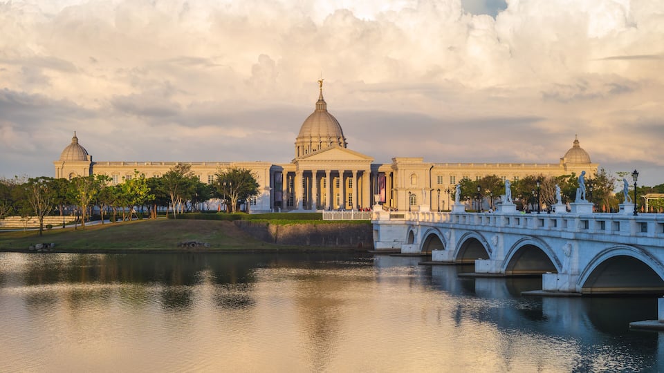 Un edificio clásico con cúpulas y columnas, un puente y un río tranquilo.