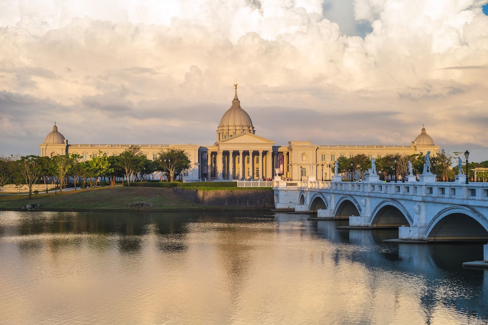 Um edifício clássico com cúpulas e colunas, uma ponte e um rio calmo.