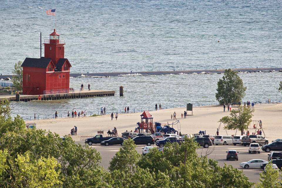 A red lighthouse, a sandy beach, and a parking lot with cars.