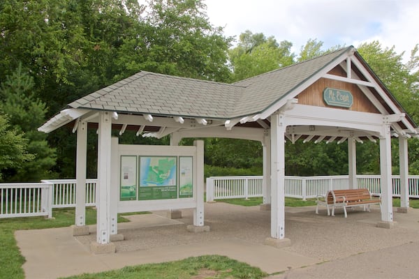 A gazebo with a sign reading "Mt. Pisgah" in a park with a white fence and green trees.