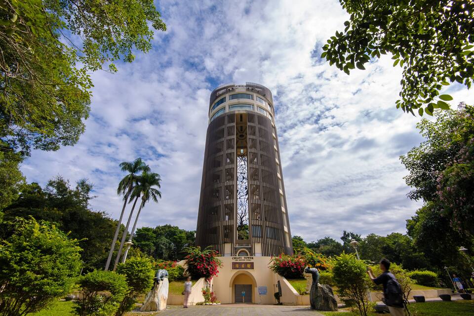 A tall, cylindrical building surrounded by lush greenery and palm trees.