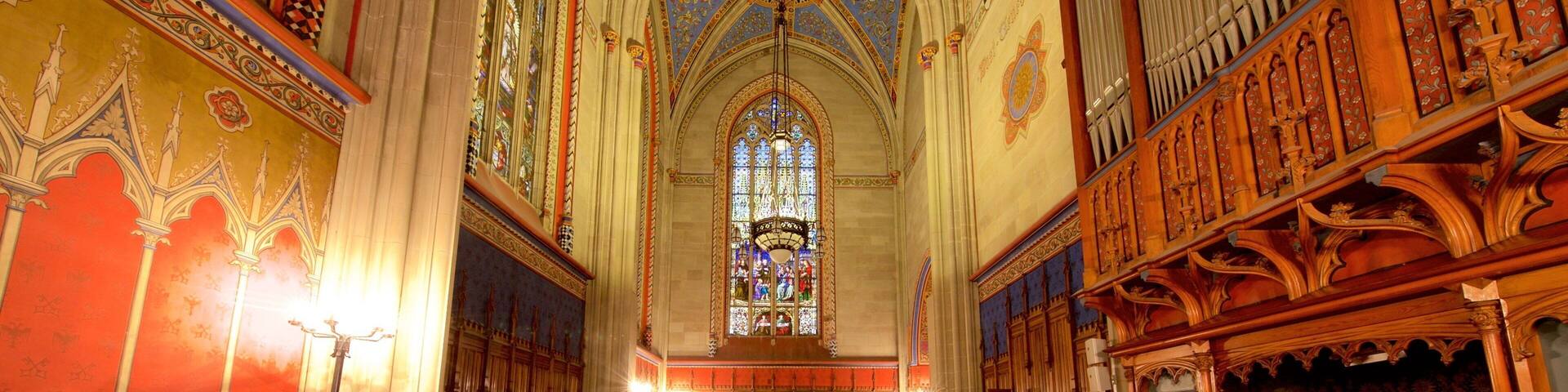 An ornate church interior with stained glass windows, wooden pews, and intricate ceiling designs.