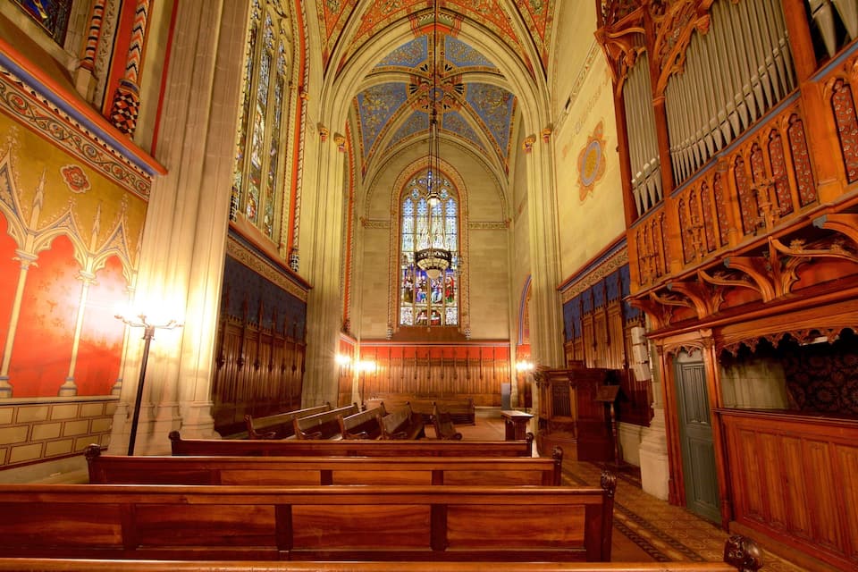 An ornate church interior with stained glass windows, wooden pews, and intricate ceiling designs.