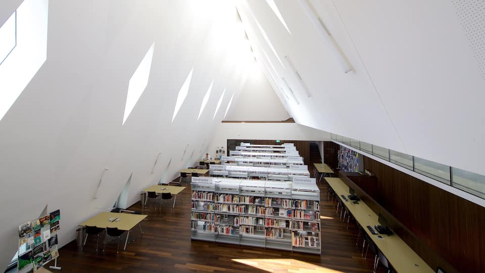 A modern library with bookshelves, tables, and a skylight.