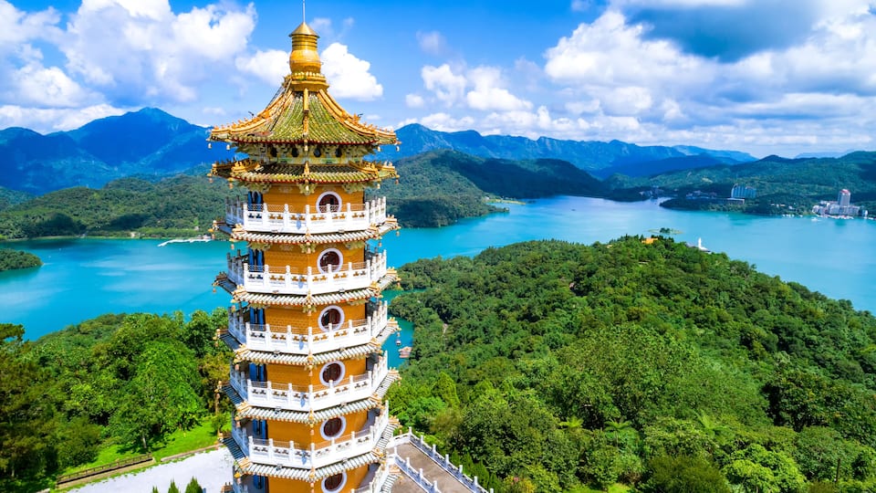 A multi-tiered pagoda with a golden roof, surrounded by lush greenery and a lake.
