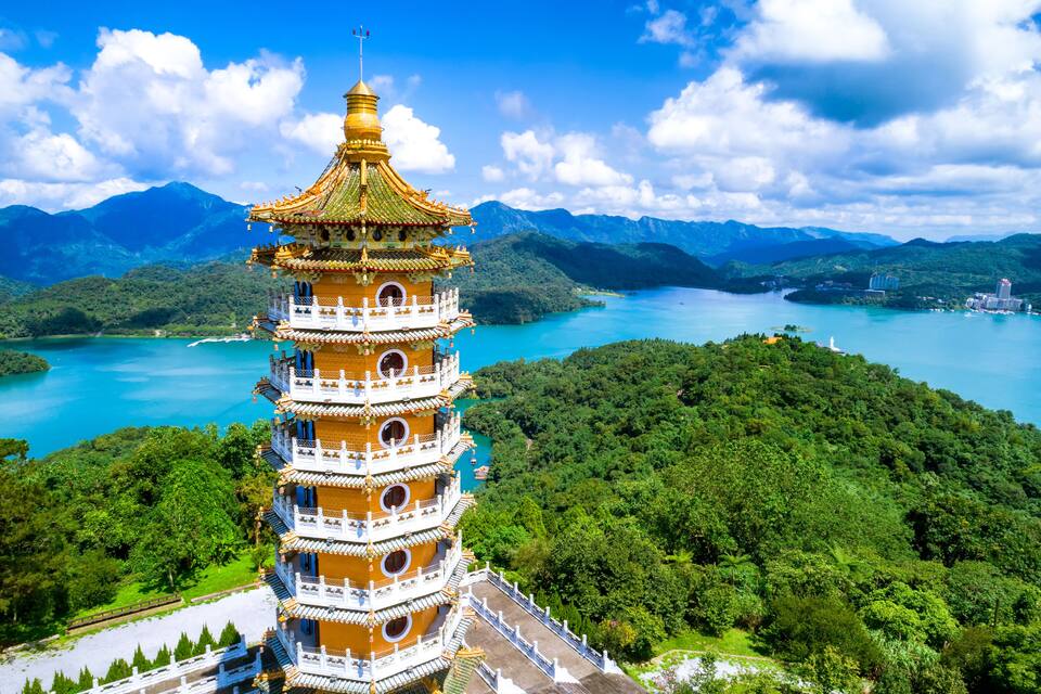 Um pagode de vários níveis com telhado dourado, cercado por vegetação exuberante e um lago.