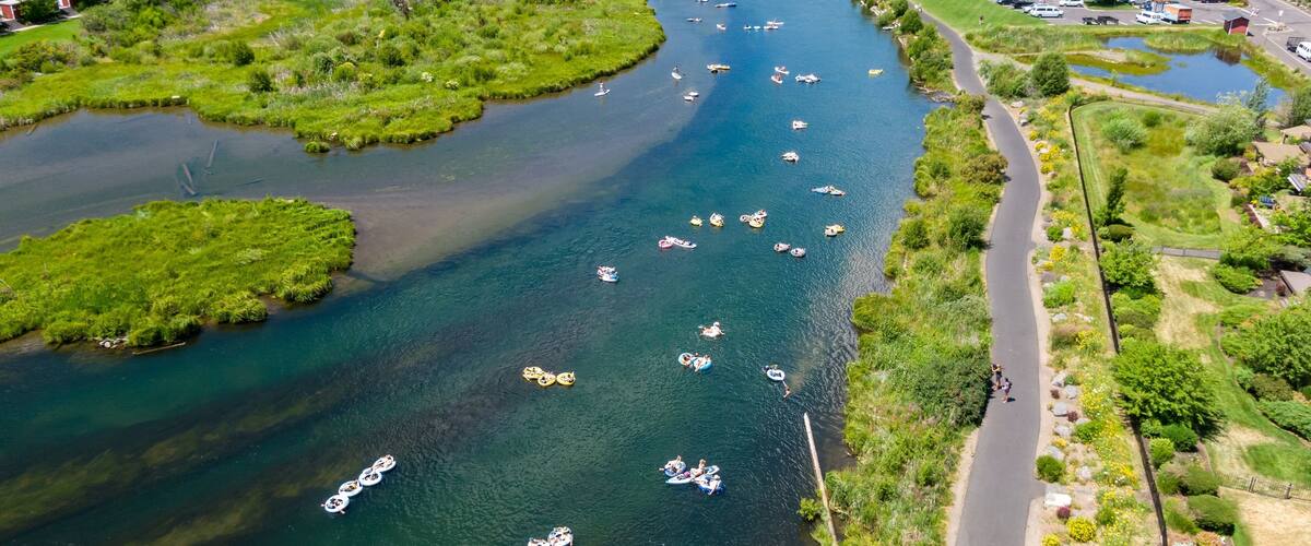 Aerial view of people tubing on the Deschutes River, enjoying a sunny day. Town and park scenery surrounds the river. Bend, Oregon, USA