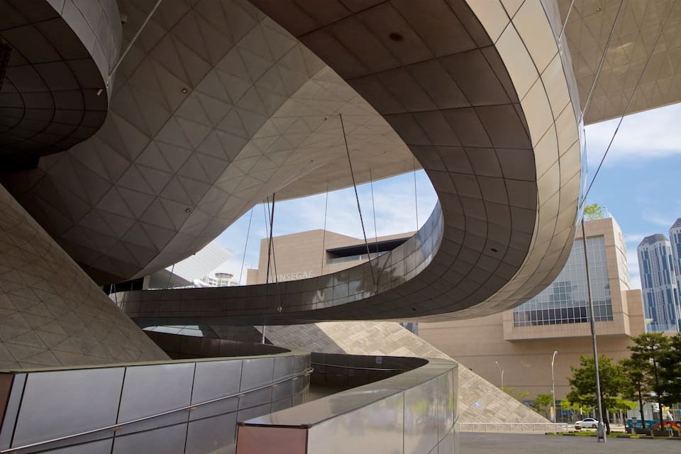 A modern architectural structure with curved metal elements and a cityscape in the background.