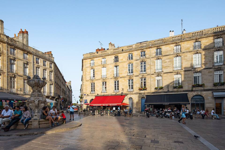 A historic square with ornate buildings, a fountain, and outdoor seating areas.