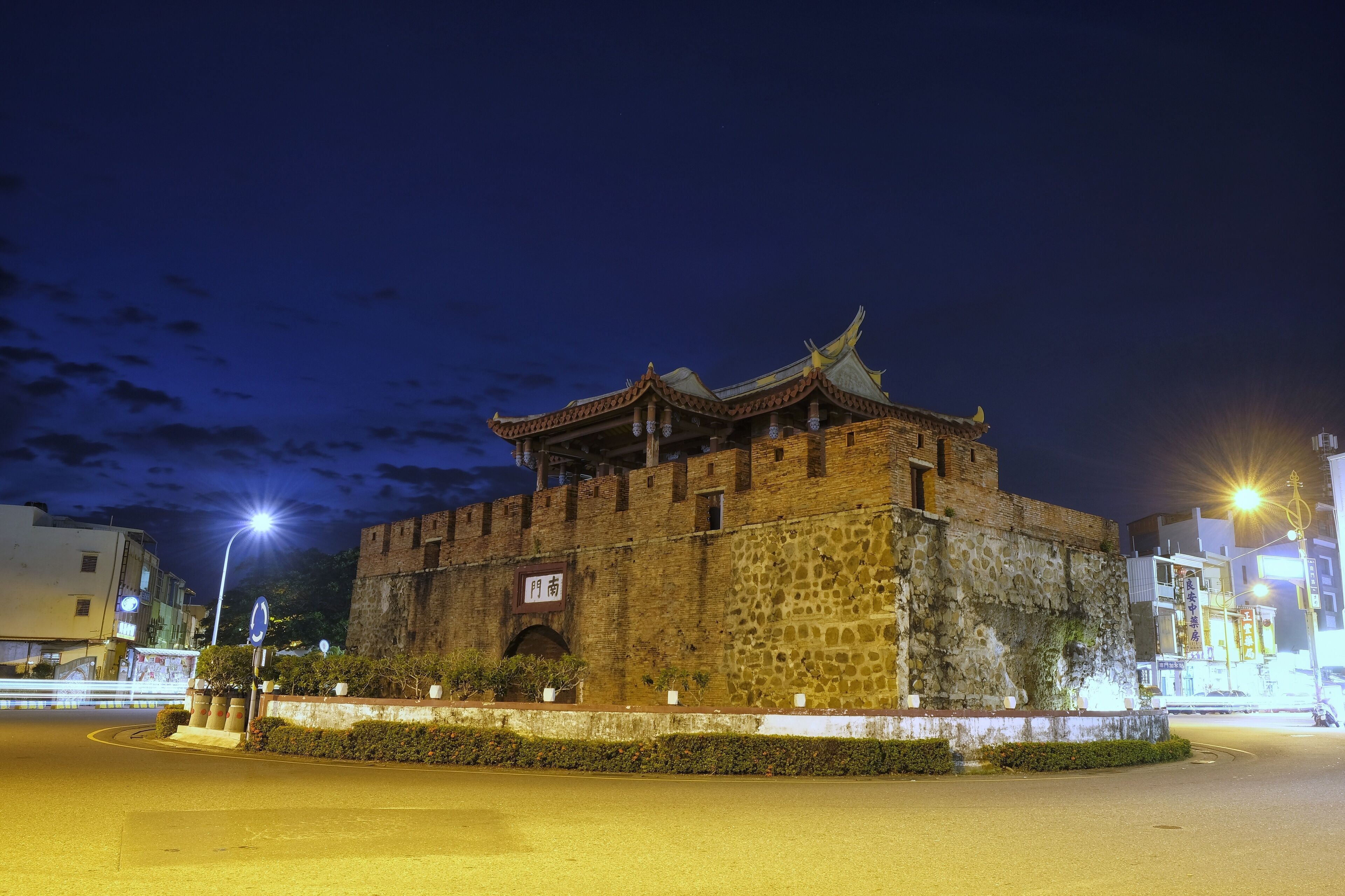 A historic stone building with traditional architecture, a well-maintained garden, and modern street lighting.