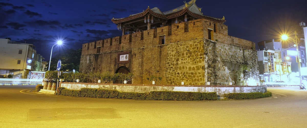 A historic stone building with traditional architecture, a well-maintained garden, and modern street lighting.
