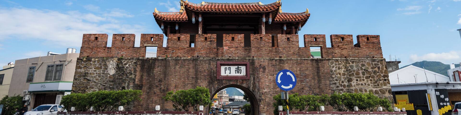 Una puerta tradicional china con techo de tejas y paredes de ladrillo, una señal de rotonda y un cielo azul despejado.