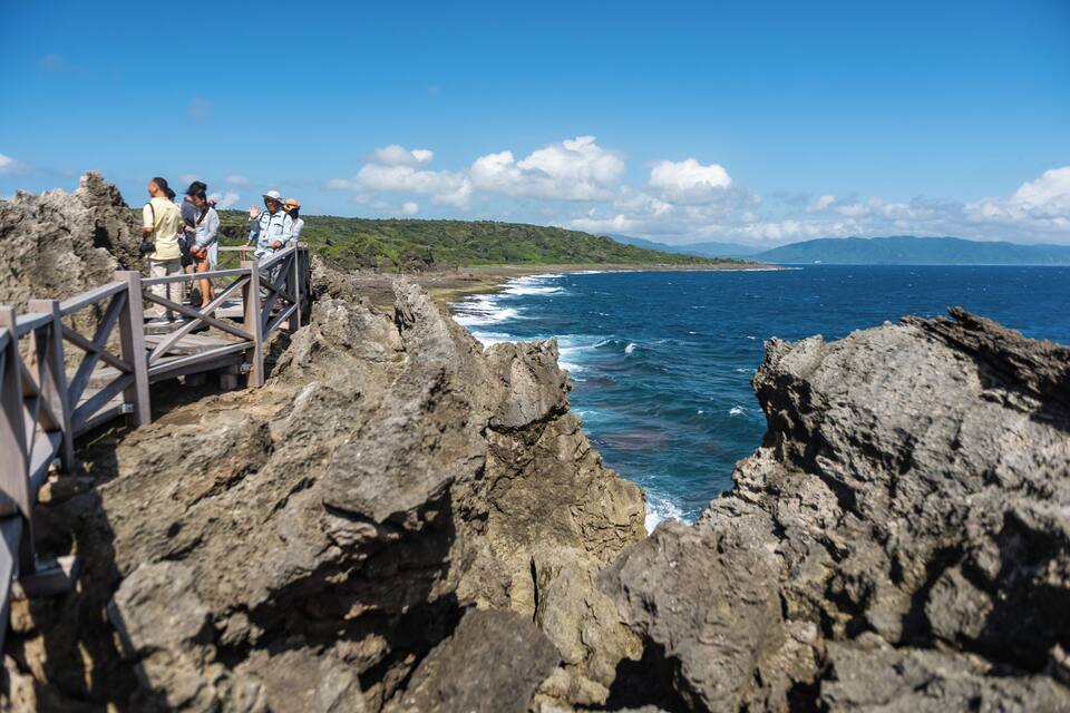 A rocky coastline with a wooden walkway and people observing the ocean.