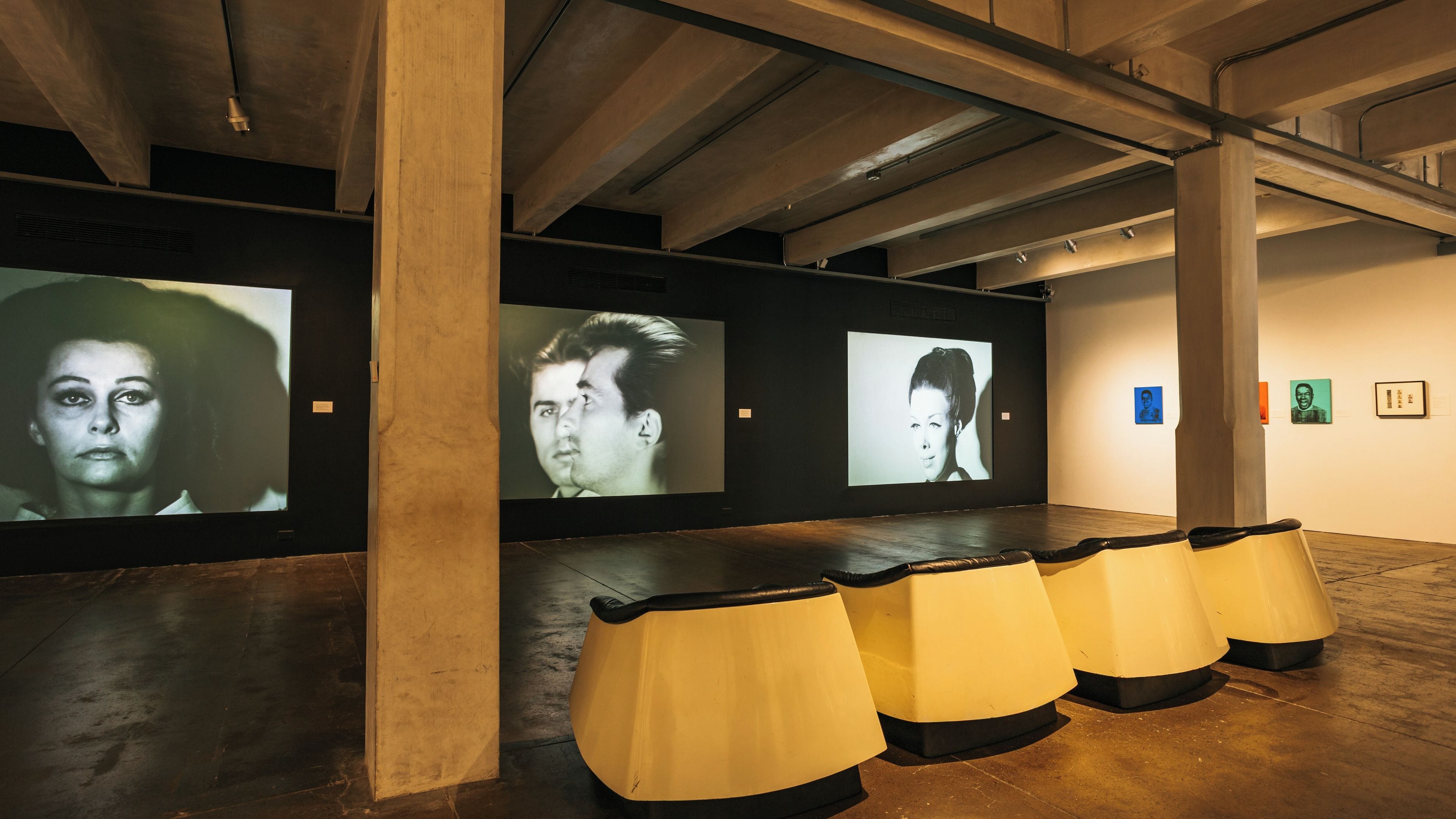 Een kunstgalerie met grote projectieschermen waarop portretten worden getoond.