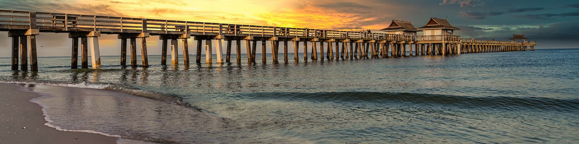 Un muelle de madera que se adentra en el mar, con un atardecer de fondo.