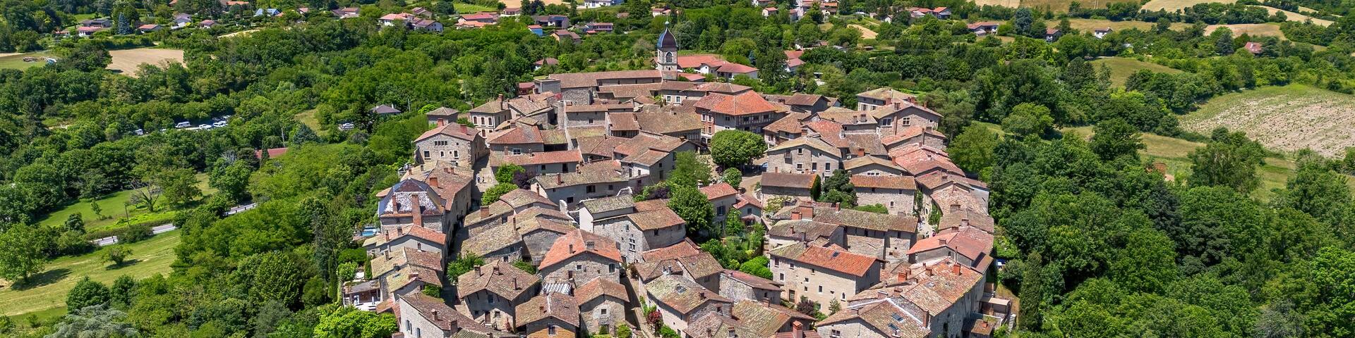 An aerial view of a historic town with a central church, surrounded by lush greenery and rolling hills.