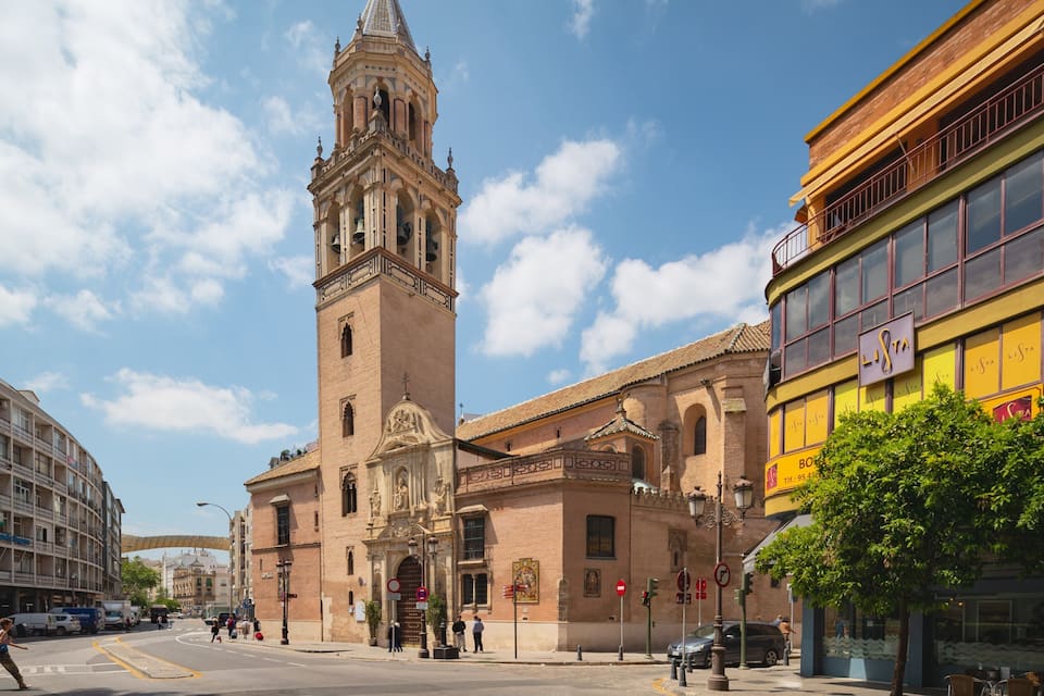 A historic church with a tall bell tower, a modern yellow building with 'LISTA' signage, and a busy street with pedestrians and vehicles.