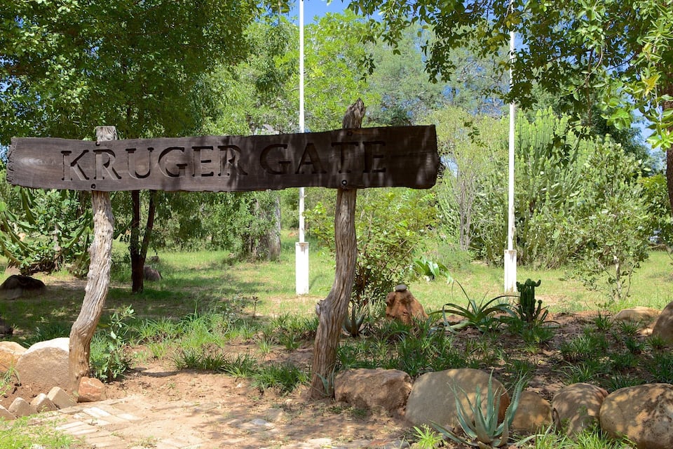 A wooden signpost with 'KRUGER GATE' written on it, surrounded by trees and rocks.
