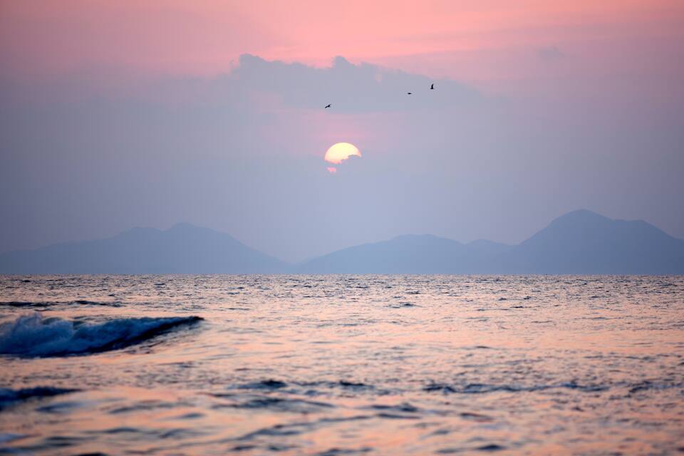 A sunset over the ocean with waves and distant mountains.