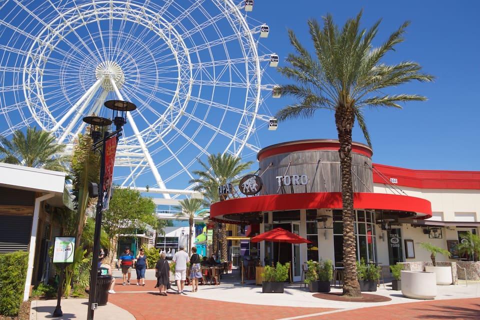 A Ferris wheel, palm trees, and a building with a red awning.