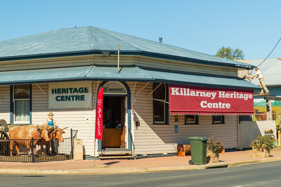 A heritage center building with a sign reading "Killarney Heritage Centre" and a statue of a man on the porch.