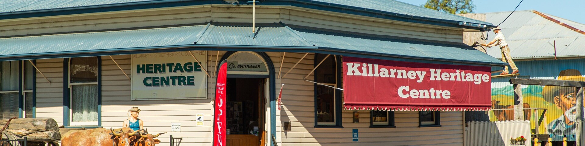 A heritage center building with a sign reading "Killarney Heritage Centre" and a statue of a man on the porch.